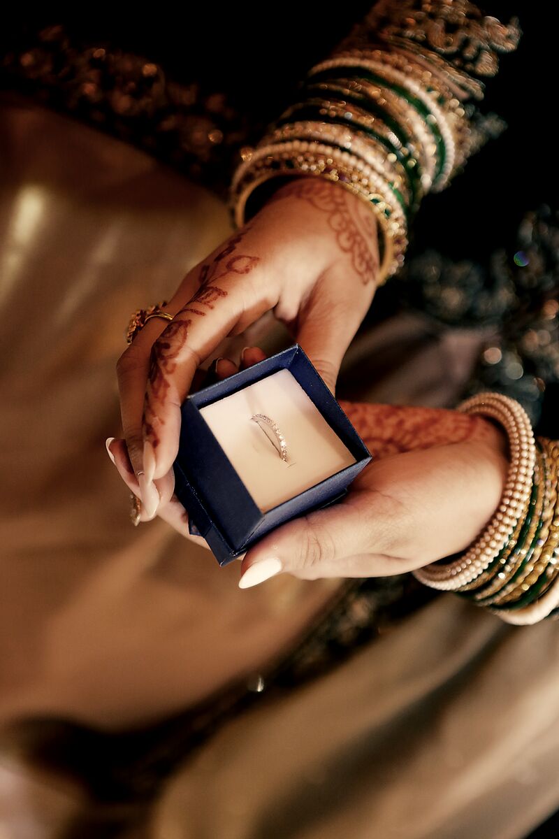 Mehndi-adorned hands in gold bangles opening a ring box